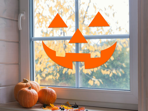 orange happy pumpkin face on a window sill next to pumpkins and fall leaves