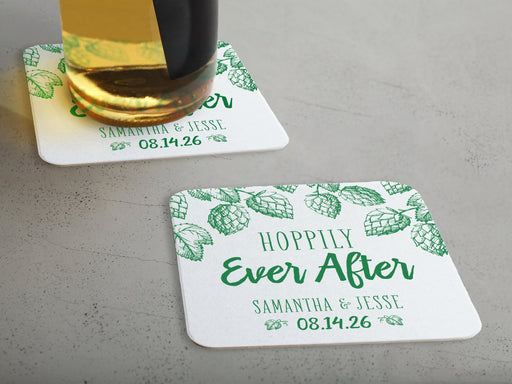 One coaster has a beer glass on it and an empty coaster sits beside it. Coasters feature Hoppily Ever After design. This design uses green lettering and sketched drawings of beer hops. Wedding couples names and date can be customized.