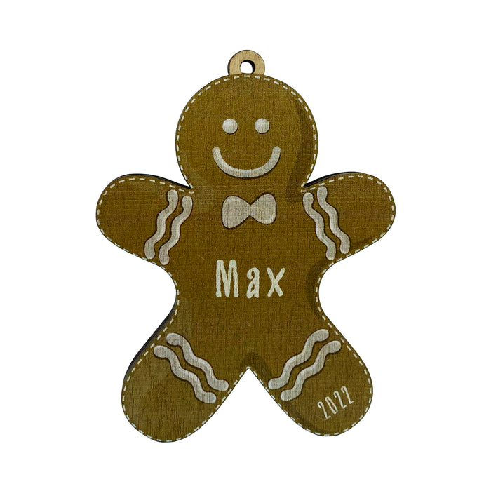 Ornament shown with Gingerbread Boy design. The ornament is wooden and shaped like a gingerbread boy. Name and year are written on ornament in white.