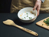 flat wooden spoon on marble counter top next to a pot of chili, herbs, lime, and a kitchen towel with an engraving on the handle that says I love you mom from Lane