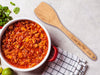 flat wooden spoon on marble counter top next to a pot of chili, herbs, lime, and a kitchen towel with an engraving on the handle that says I love you mom from Lane