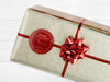 A gold foil cardstock Santa gift tag is shown on a craft paper wrapped box. The box also has a red and white striped string on it. The box is seen on a wooden surface.