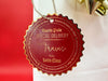 A gold foil cardstock Santa gift tag is shown hanging on a white gift bag. The bag is on a red backdrop and has a gold bow on it.