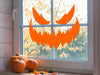 scary orange pumpkin face vinyl sticker on window next to pumpkins and fall leaves