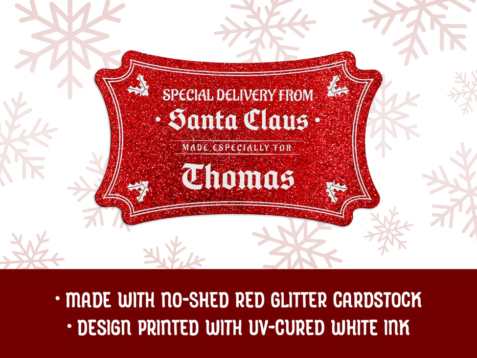 A red glitter cardstock Santa gift tag is shown on a white background with red snowflakes. Text underneath the tag reads: Made with no-shed red glitter cardstock, Design printed with UV-cured white ink.