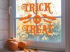 orange trick or treat vinyl sticker on an interior window next to pumpkins and fall leaves